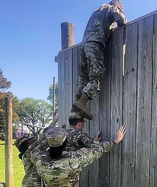 ROTC climbing over wooden wall.